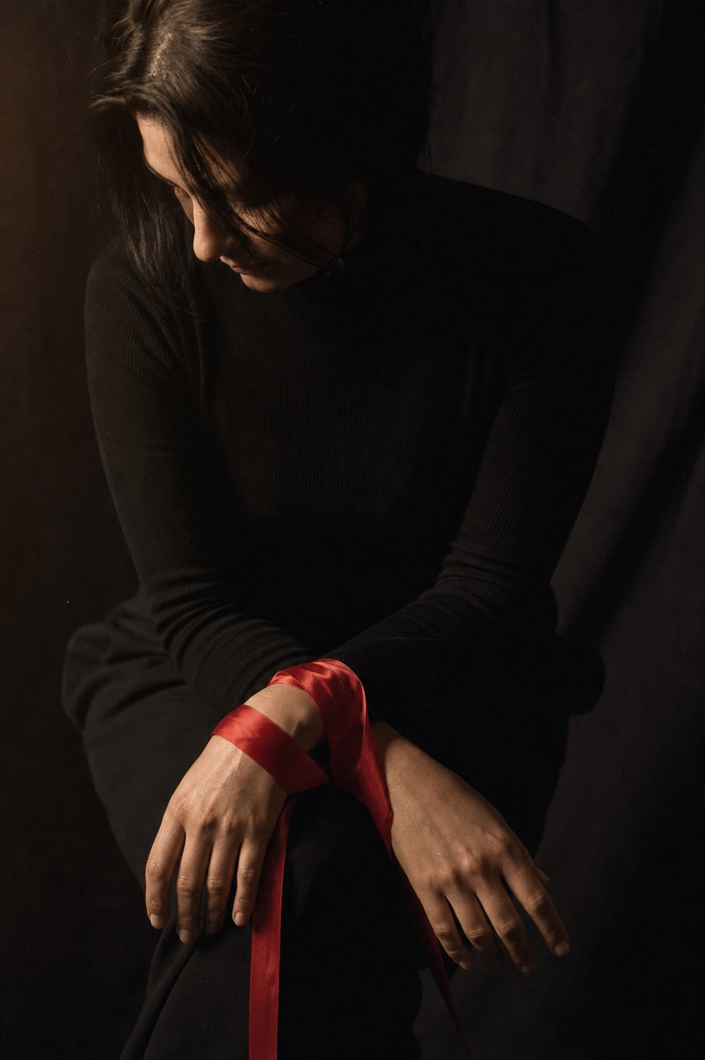 A clothed adult with a loose red silk ribbon across their wrists for a soft BDSM beginner guide