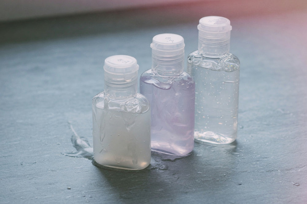 A dark bottle of personal lubricant and a folded black cloth on a low bedside surface — ready for anal play, no product logos