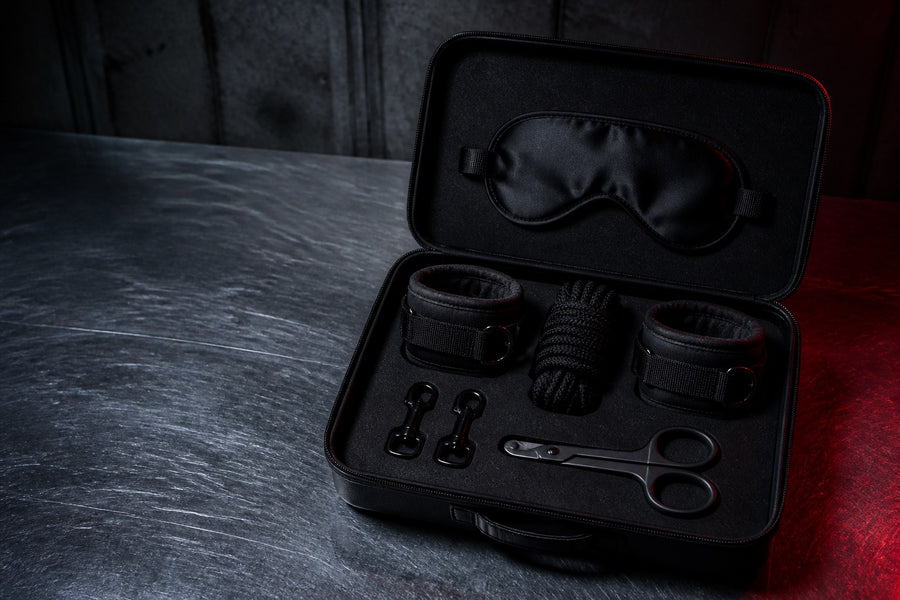 Open black bondage kit with cuffs, blindfold, rope, clips, and safety shears