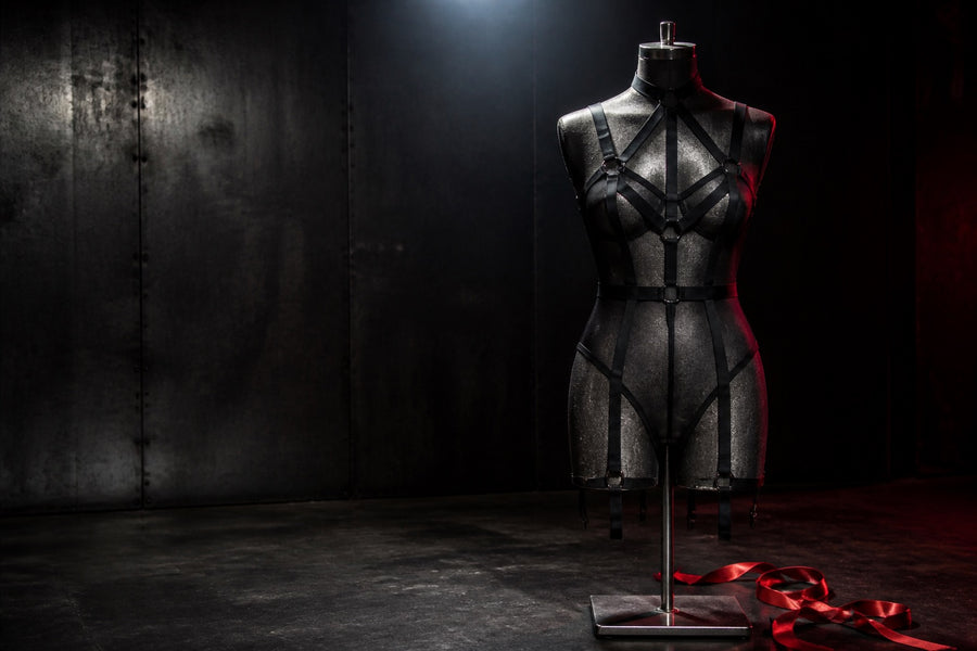 Empty black mesh bodice and geometric harness on a steel dress form under red light