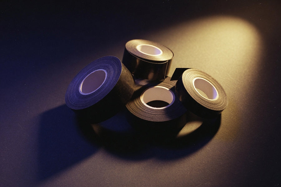 A roll of matte black self-adhesive bondage tape and safety scissors on dark fabric — restraint gear, not household duct tape