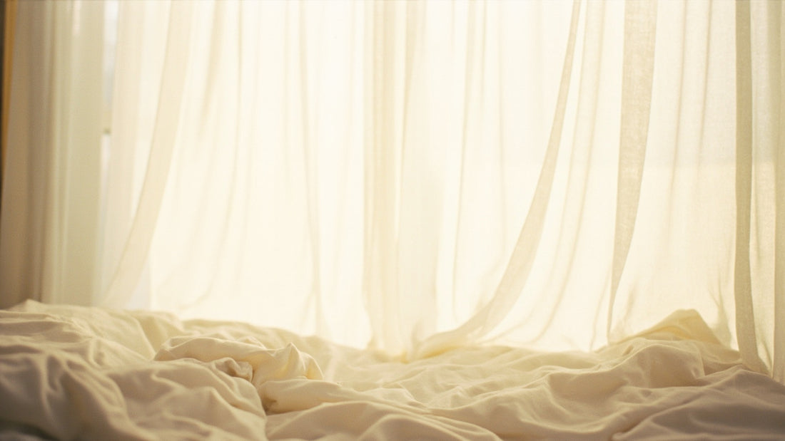 A dim, film-grain bedroom still — soft folded sheets and low light, no faces — set for an unhurried first time