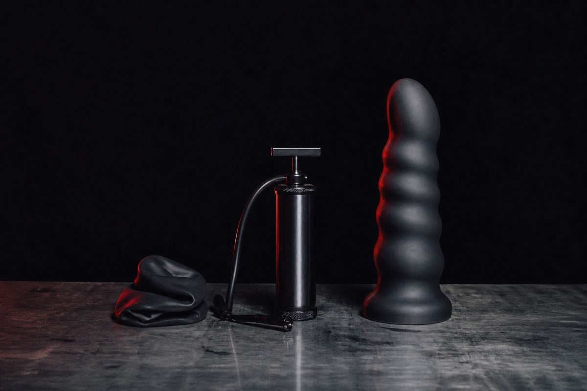 Collapsed and expanded black inflatable dildo forms beside a hand pump